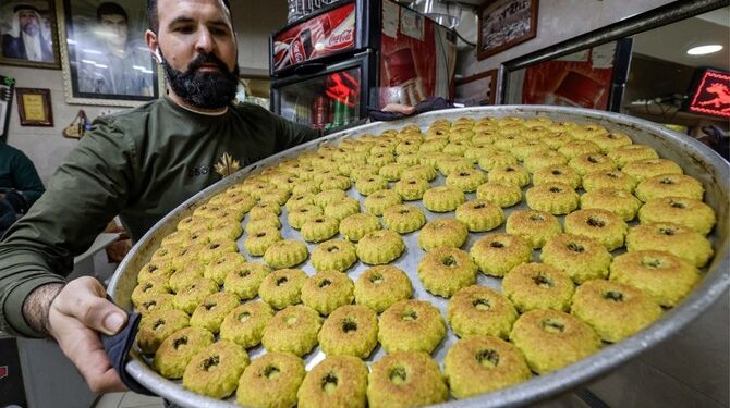 A Palestinian baker carries a tray of fresh "maamoul", traditional pastries filled with dates or nuts, on the eve of Eid al-Fitr at the end of Muslim holy month of Ramadan, in Jerusalem on April 20, 2023. (Photo by AHMAD GHARABLI / AFP)